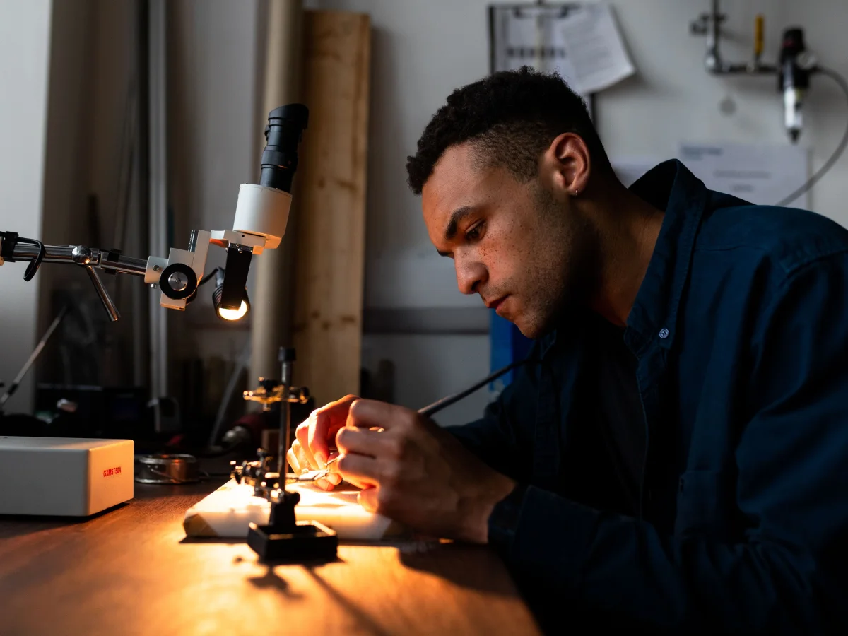 An engineer working on electronic components under a microscope and task lighting